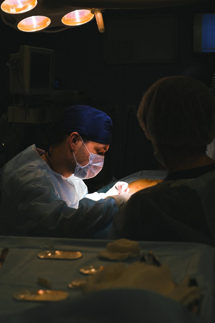 about-us A surgeon in an operating room focused on a procedure under surgical lights.